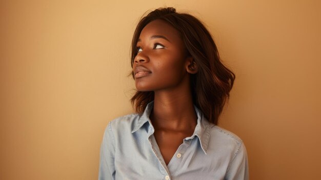 joven africana mirando hacia arriba con una expresión reflexiva usando una camisa azul claro contra un fondo bronceado