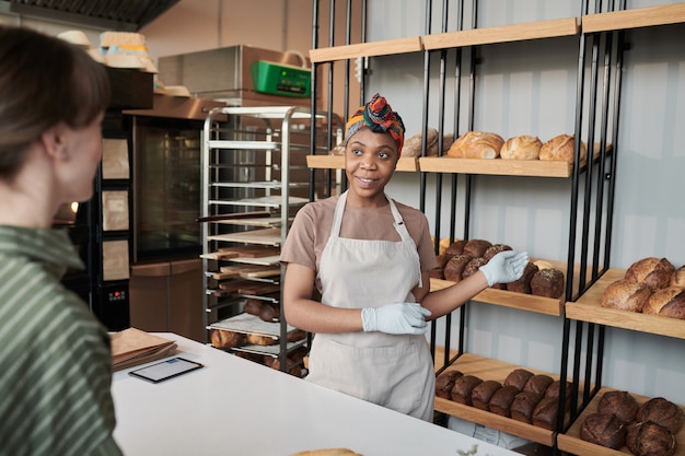 Joven africana mostrando el pan fresco al cliente en la panadería