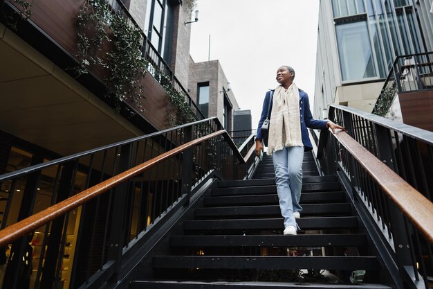 Joven africana con el pelo corto viste ropa de moda bajando las escaleras