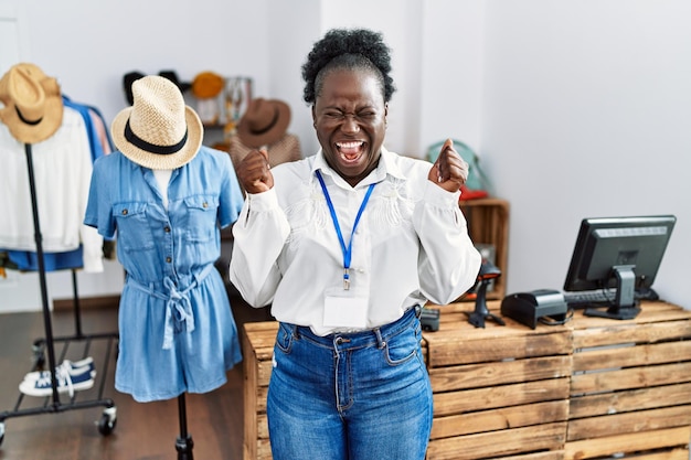 Joven africana que trabaja como gerente en una boutique minorista emocionada por el éxito con los brazos levantados y los ojos cerrados celebrando la victoria sonriendo el concepto de ganador