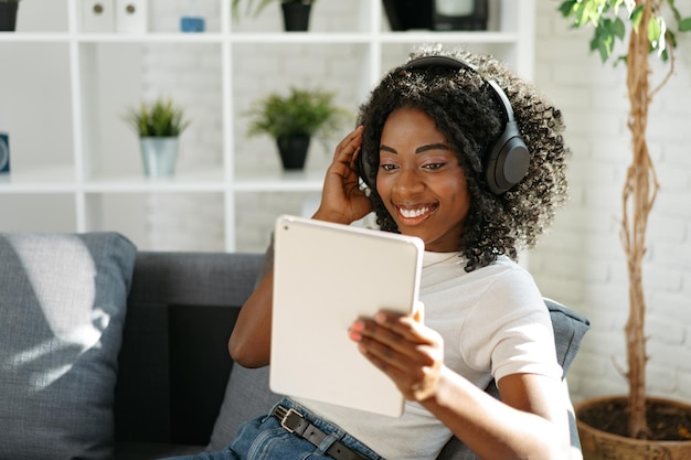 Joven africana usando tableta digital y sonriendo mientras descansa en casa