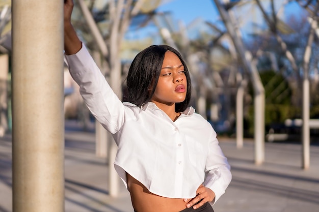 Joven africana vestida de blanco en la ciudad al atardecer haciendo una pose de moda mirando a la derecha