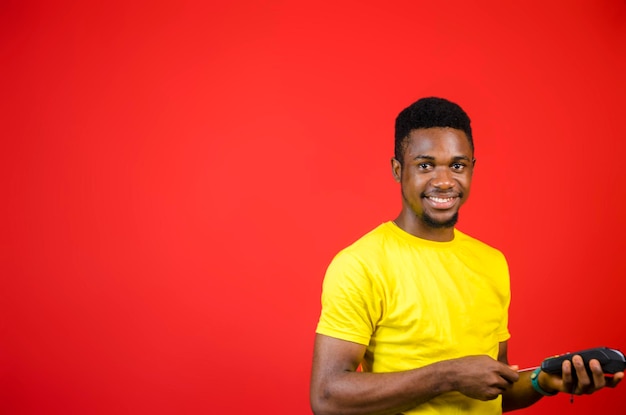 Un joven africano apuesto que usa tela amarilla se siente emocionado mientras sostiene su máquina de punto de venta