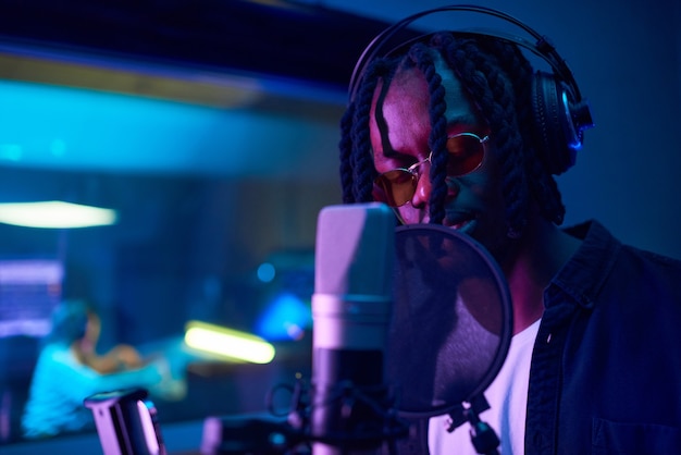 Joven africano en auriculares grabando una nueva canción en el estudio de música