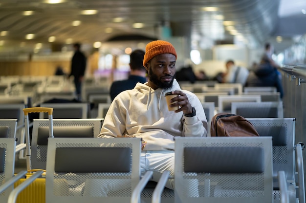 Joven africano bebiendo café y comiendo sándwich mientras espera volar en la terminal del aeropuerto