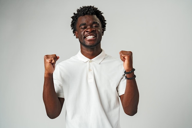 Un joven africano con camisa blanca celebra con una bomba de puño alegre sobre un fondo gris