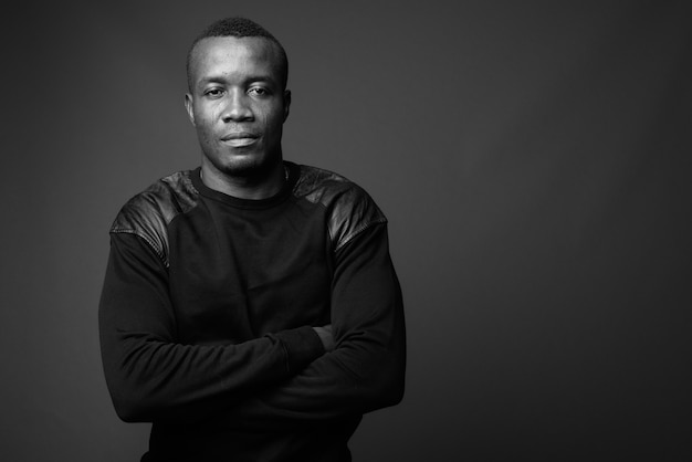 Foto joven africano con camisa negra de manga larga contra la pared gris. en blanco y negro