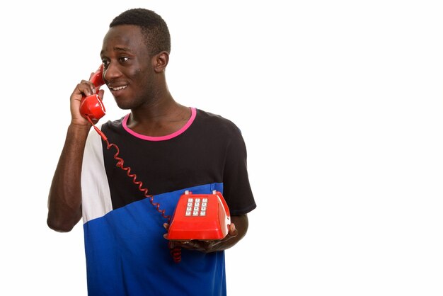Joven africano feliz sonriendo y hablando por teléfono antiguo