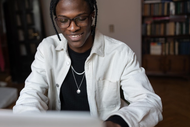 Un joven africano feliz y sonriente con gafas que usa una computadora portátil en casa y pasa su tiempo libre en Internet