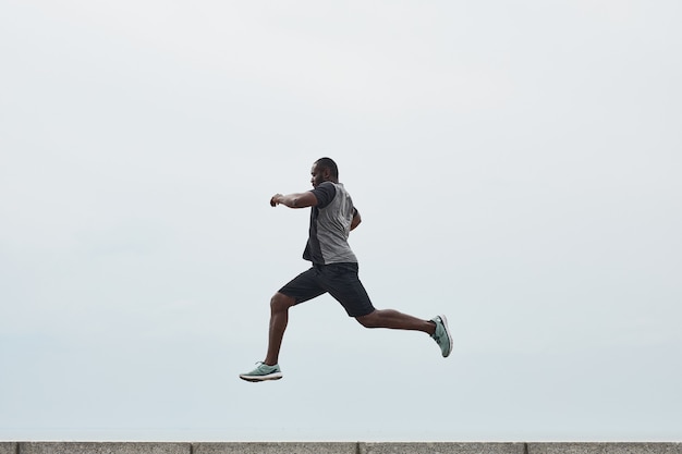 Joven africano haciendo ejercicio al aire libre él saltando por encima de una barrera