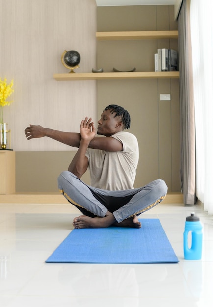 Joven africano haciendo ejercicios de yoga en la sala de estar de su casa con el placer