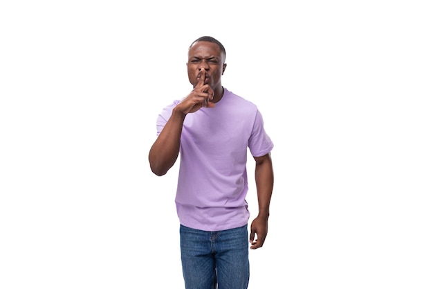 Joven africano inteligente vestido con una camiseta lila y jeans pensando en un fondo blanco