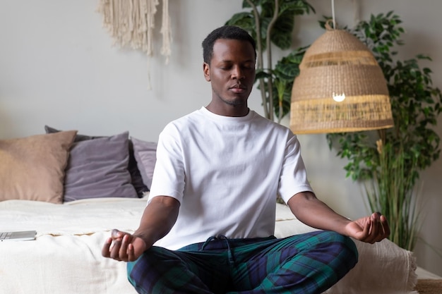 Joven africano meditando sentado en su dormitorio por la mañana