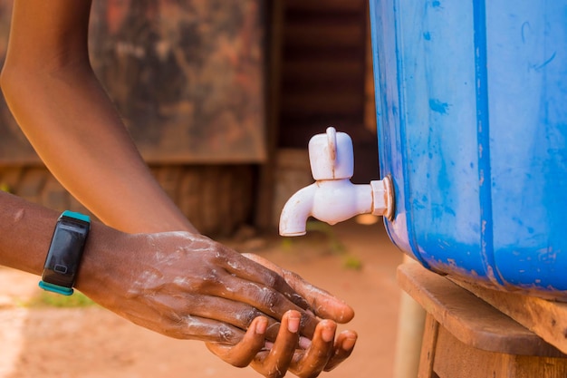 Joven africano negro lavándose las manos con jabón bajo un grifo de agua