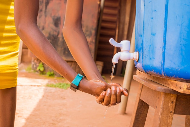 Joven africano negro lavándose las manos con jabón bajo un grifo de agua