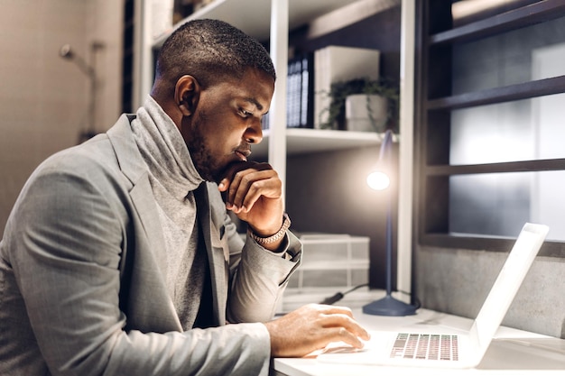 Joven africano negro que se relaja usando la tecnología de la computadora portátil mientras está sentado en la mesa Joven africano creativo trabaja y escribe en el teclado en la tarea en el concepto de casa