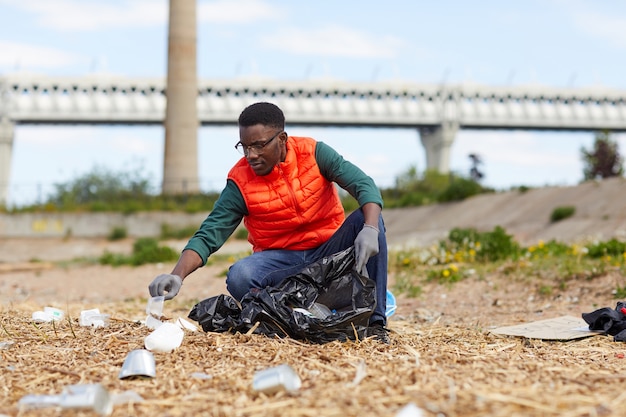 Joven africano recogiendo la basura en las bolsas al aire libre