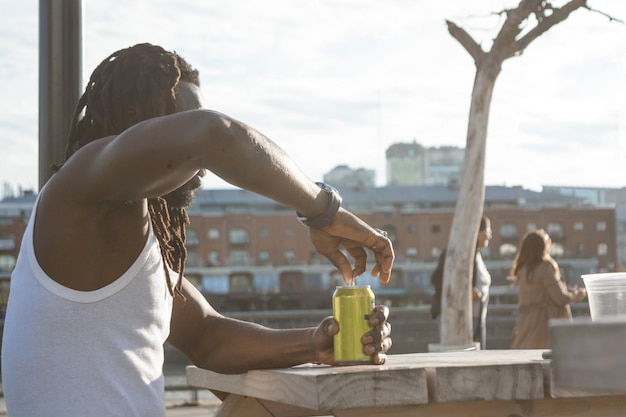 Joven africano sentado al aire libre abriendo un refresco