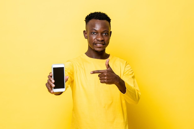 Un joven africano sonriente apuntando a un teléfono móvil con un fondo de estudio amarillo