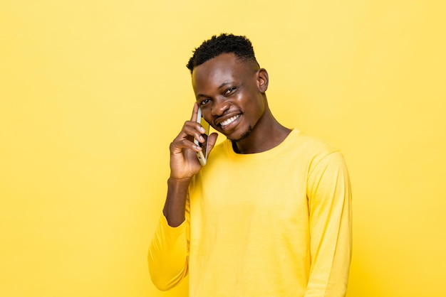 Un joven africano sonriente hablando por teléfono móvil con un fondo de estudio aislado amarillo