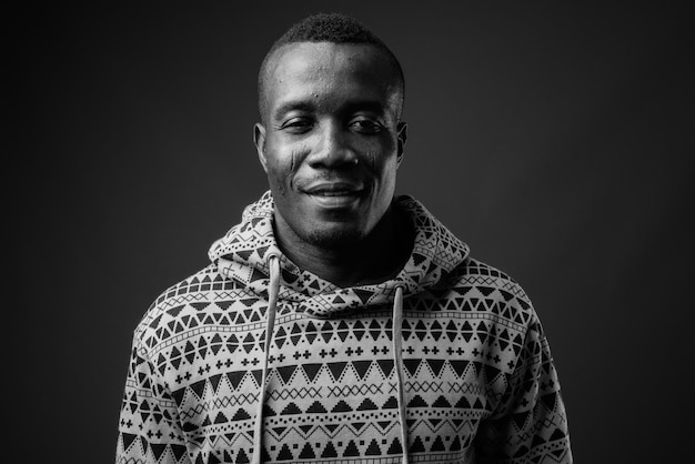 joven africano con sudadera con capucha contra la pared gris. en blanco y negro