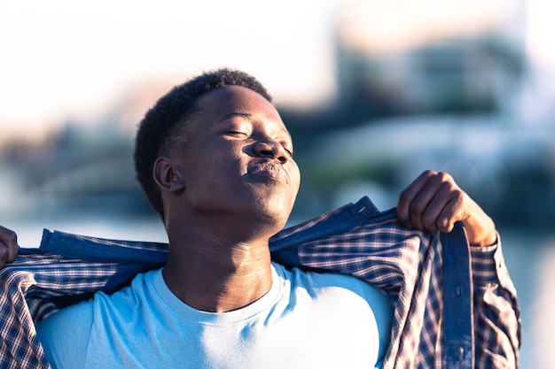 Joven africano tomando un baño de sol mientras se quita la camiseta al aire libre