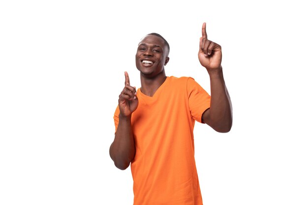 Un joven africano vestido con una camiseta naranja sonriendo lindamente y experimentando la felicidad en un blanco