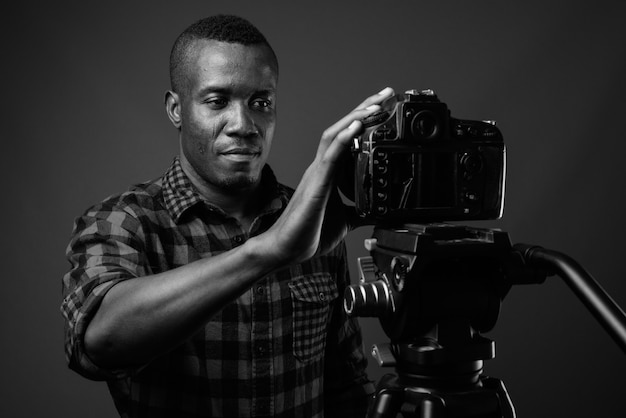 joven africano vlogging mientras usa camisa a cuadros contra la pared gris. en blanco y negro