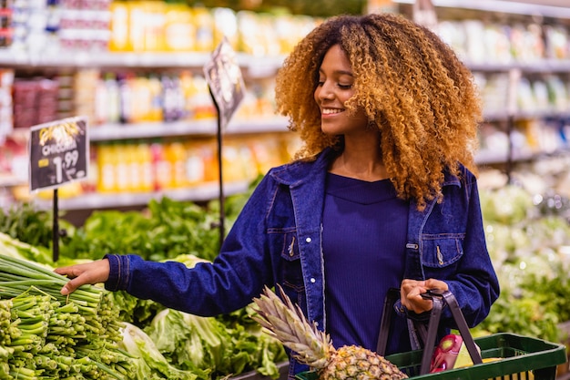 Joven afro comprando frutas y verduras en el supermercado.