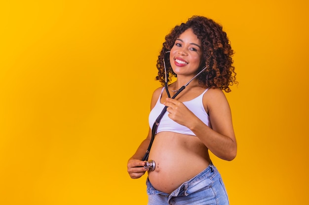 Una joven afro embarazada con estetoscopio escuchando al bebé