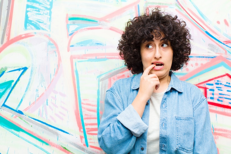 Foto joven afro con mirada sorprendida, nerviosa, preocupada o asustada, mirando hacia el lado hacia el espacio de copia en la pared de graffiti