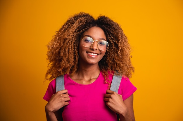 Joven afro con mochila en la espalda sobre fondo amarillo. Joven estudiante sonriendo con gafas