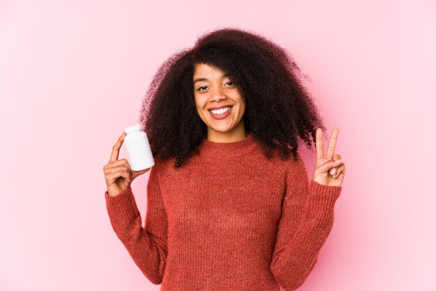 Joven afro mujer sosteniendo una vitaminas aisladas Joven afro mujer sosteniendo una vitaminashowing número dos con los dedos.