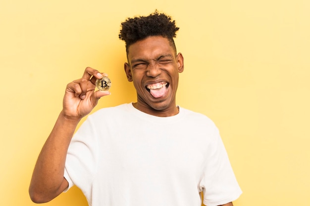 Joven afro negro con actitud alegre y rebelde bromeando y sacando la lengua concepto bitcoin