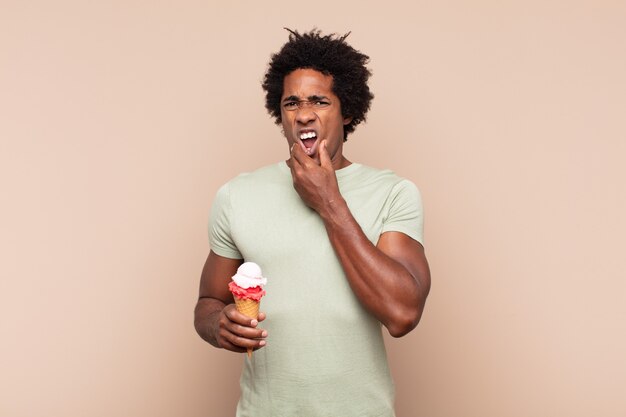 Joven afro negro con la boca y los ojos bien abiertos y la mano en la barbilla, sintiéndose desagradablemente conmocionado, diciendo qué o guau