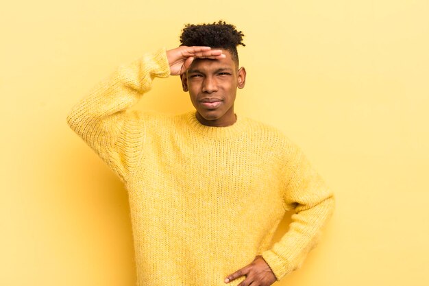 Joven afro negro que parece desconcertado y asombrado con la mano sobre la frente mirando lejos mirando o buscando