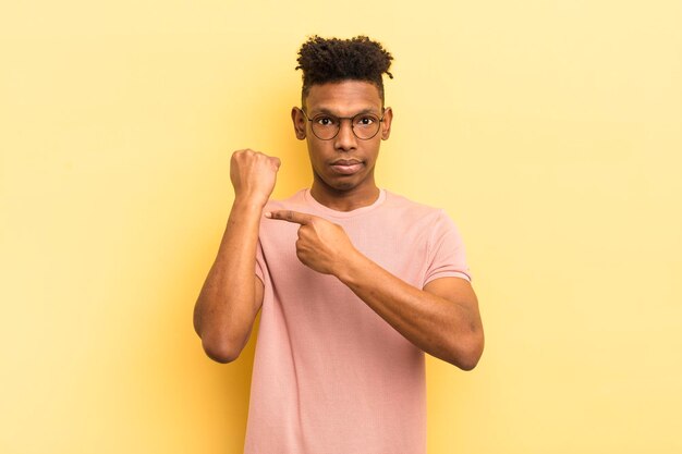 Joven afro negro que parece impaciente y enojado señalando el reloj pidiendo puntualidad quiere llegar a tiempo