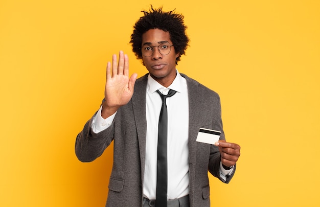 Joven afro negro que parece serio, severo, disgustado y enojado mostrando la palma abierta haciendo gesto de parada