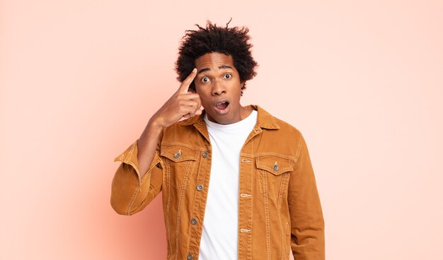 Joven afro negro que parece sorprendido, con la boca abierta, conmocionado, dándose cuenta de un nuevo pensamiento, idea o concepto