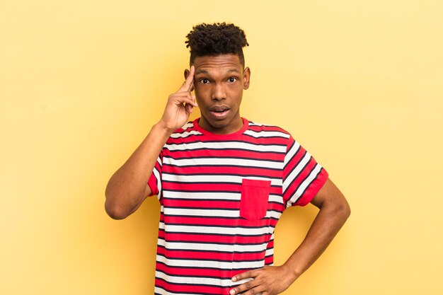 Joven afro negro que parece sorprendido con la boca abierta sorprendido al darse cuenta de una nueva idea o concepto de pensamiento