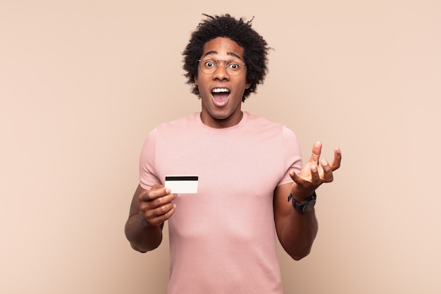 Joven afro negro que se siente extremadamente conmocionado y sorprendido, ansioso y en pánico, con una mirada estresada y horrorizada