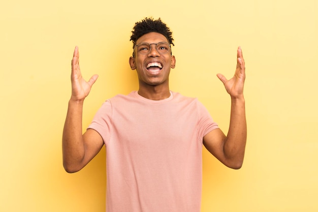 Joven afro negro que se siente feliz, asombrado, afortunado y sorprendido celebrando la victoria con ambas manos en el aire