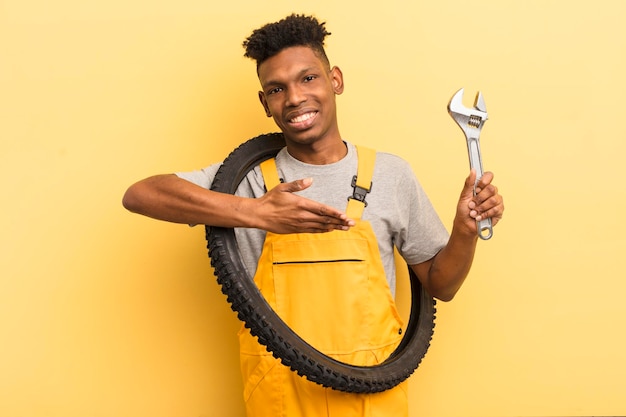 Joven afro negro sonriendo alegremente sintiéndose feliz y mostrando un concepto de mecánico de bicicletas