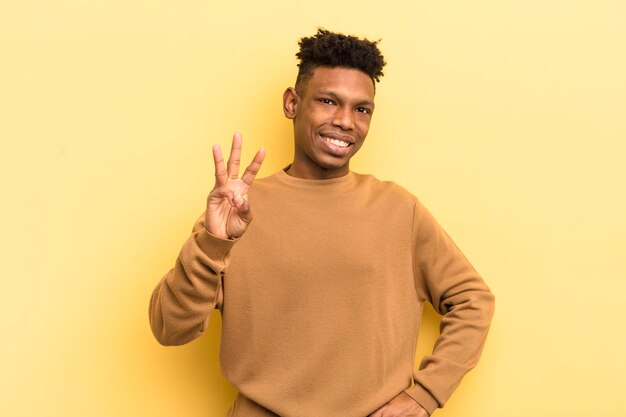 Joven afro negro sonriendo y luciendo amigable mostrando el número tres o tercero con la mano hacia adelante contando hacia atrás