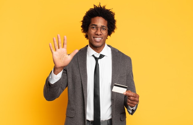 Joven afro negro sonriendo y luciendo amistoso, mostrando el número cinco o quinto con la mano hacia adelante, contando hacia atrás