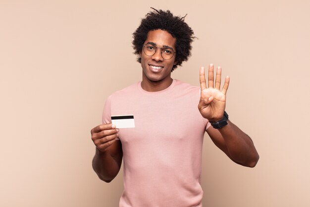 Joven afro negro sonriendo y mirando amigablemente, mostrando el número cuatro o cuarto con la mano hacia adelante, contando hacia atrás