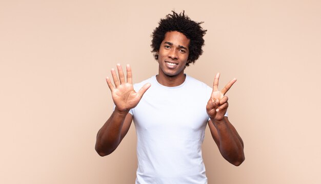 Joven afro negro sonriendo y mirando amistosamente, mostrando el número ocho u octavo con la mano hacia adelante, contando hacia atrás