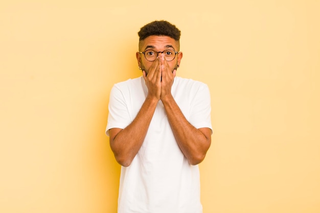 Joven afro que parece feliz, alegre, afortunado y sorprendido cubriendo la boca con ambas manos