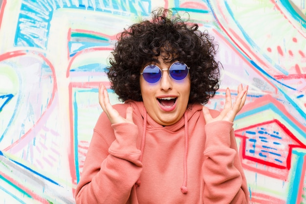 Foto joven afro se siente sorprendida y emocionada, riendo, asombrada y feliz por una sorpresa inesperada en la pared de graffiti