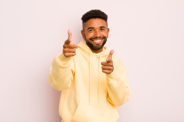 Joven afro sonriendo con una actitud positiva y feliz apuntando a la cámara haciendo señales de armas con las manos